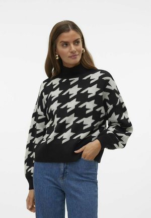 Zwart-wit houndstooth gebreid sweater met lange mouwen en een hoge kraag, gemaakt van een zacht breimateriaal, gecombineerd met blauwe jeans.