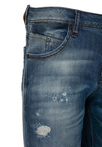 Blauwe denim jeans met versleten details, zichtbaar rafelen en lichte vervaging. Klassiek vijf-pocket ontwerp met contrasterende stiksels en knoopsluiting.