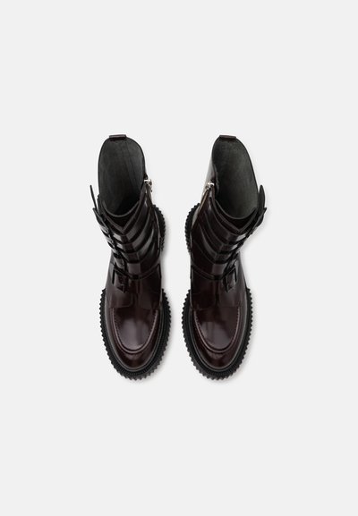 Botine din piele burgundă închisă cu un finisaj lucios, curele suprapuse și talpă din cauciuc cu un model texturat.