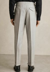 Grey plaid trousers with a relaxed fit, featuring pleats, a back pocket, and finished hemlines paired with black shoes.