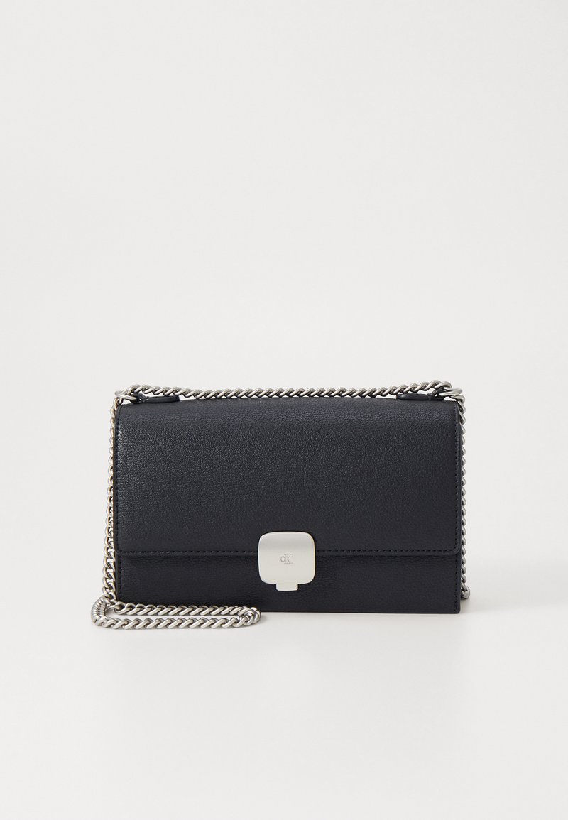 Bolsa transversal preta em couro com uma alça de corrente prateada, apresentando um fecho de clasp na parte frontal e uma textura suave. Forma retangular compacta.