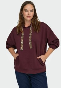 Bordo puloveris ar kapuci, ar leopardu rakstu stīgas, brīvs piegriezums un sānu kabatām. Kokvilnas maisījuma materiāls ar gludu tekstūru.