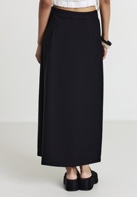Schwarzer Maxikleid, glatter Stoff, A-Linie Silhouette, elastischer Bund, knöchellang, getragen mit Plateauschuhen, minimalistisches Design.