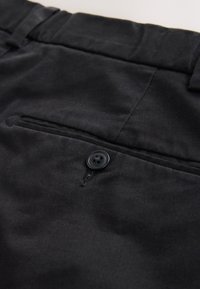 Pantalon en tissu noir avec une poche avant et un bouton noir à quatre trous, texture lisse et coupe ajustée.