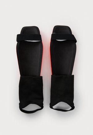 Svarte beskyttende leggskinn med røde detaljer, med en myk innerfôr og justerbare borrelåsremmer for sikker passform.