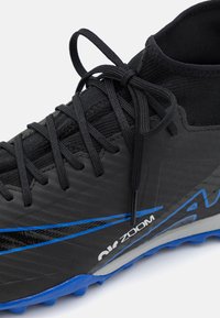 Černá sportovní bota s texturovaným svrškem, modrými akcenty a designem vysokého střihu. Obsahuje podrobné šněrování a vzorovanou gumovou podrážku.