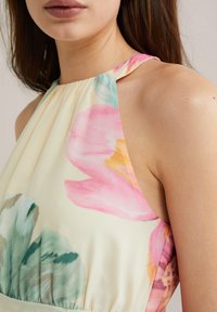 Kukkamekko, jossa on halterneck-muotoilu ja pastellivärejä. Kangas on pehmeä ja siinä on vaaleanpunaisia ja vihreitä akvarellikuvioita.