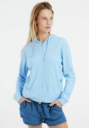 Hellblauer Reißverschluss-Hoodie aus weichem Stoff, mit vorne senkendem Reißverschluss, Kordelzugkapuze und langen Ärmeln, kombiniert mit Jeansshorts.