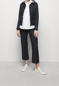 Námořnická prošívaná bunda se šedou kapucí, bílá košile na knoflíky, tmavé zkrácené džíny a bílé tenisky s hnědým akcentem. Neformální outfit.