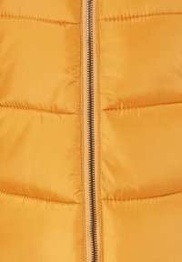 Gul pufferjakke med en glat, blank overflade og vertikal quiltet design. Central sort lynlås fremhævet af orange syninger.