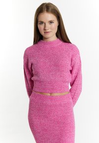 Top a coste rosa con un collo alto e maniche lunghe, abbinato a una gonna attillata in tinta unita con una texture simile.
