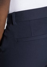 Navy blue trousers made of textured fabric, featuring a side pocket and a smooth waistband, showing clean lines and tailored design details.