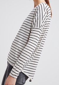 Lange mouwen shirt in crème met verticale zwarte strepen, voorzien van een relaxte pasvorm en een afgeronde zoom, gemaakt van zacht textielmateriaal.