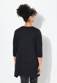 Tunika nera a maniche lunghe con scollatura rotonda, spacchi laterali e vestibilità ampia. Il tessuto ha una consistenza morbida, adatta per un abbigliamento casual.