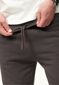 Dunkelgraue Jogginghose mit einem elastischen Bund und einer Kordel. Der Stoff wirkt weich und glatt, mit einer figurschmeichelnden Passform um die Taille.