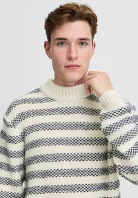 Pulover tricotat cu guler cu nervuri, având dungi orizontale crem și bleumarin, model texturat și croi lejer.