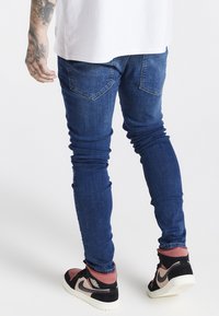 Jeans de denim azul ajustados con una textura suave, dos bolsillos traseros y un desvanecimiento sutil. Combinados con unas zapatillas altas en negro y rosa.