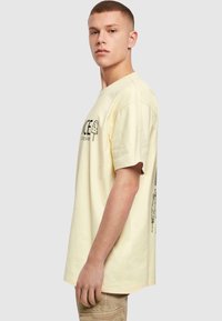 Gul bomulds T-shirt med et sort grafisk design af is-sodavand. Korte ærmer og en afslappet pasform med en glat tekstur.