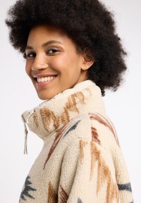 Fleecejacke mit hohem Kragen in Creme, mit abstrakten braunen und blauen Mustern, Reißverschluss und strukturierter Oberfläche.
