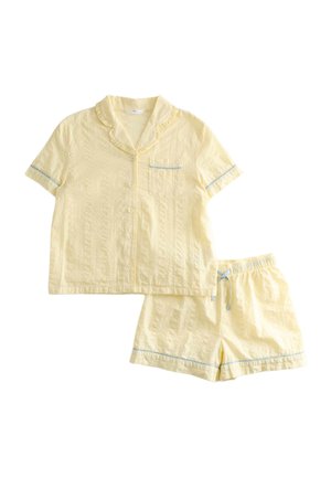 Kortærmet gul pyjamasæt med skjorte med knapper, der har flæsekant på kraven og brystlomme, kombineret med shorts med elastisk talje og blå kant.