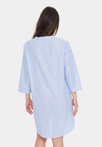 Ljusblå randig kaftan-klänning med trekvartslånga ärmar, en enkel krage och rak skärning, tillverkad av ett texturerat tyg.