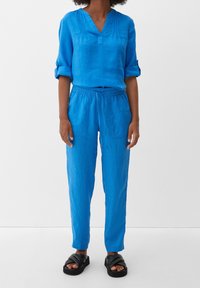 Blå linningstopp med V-hals och uppvikt ärm, kombinerad med matchande byxor med elastisk midja och svarta sandaler.