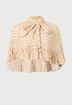 Μπεζ διάφανη μπλούζα με μαύρα πουά, ψηλός λαιμός δεμένος με φιόγκο και στρώσεις βολάν στο τελείωμα.