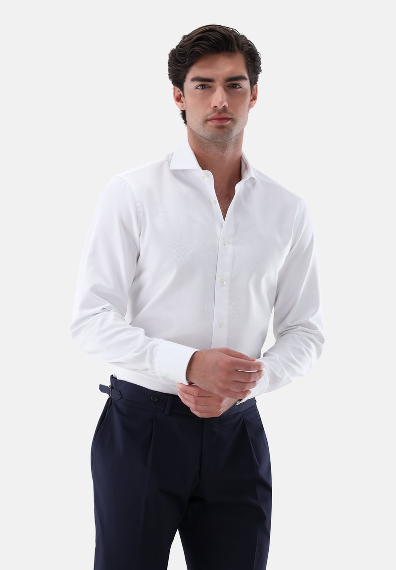 Camicia bianca a maniche lunghe con motivo testurizzato, apertura con bottoni e colletto a punta, abbinata a pantaloni blu navy con regolatori laterali.