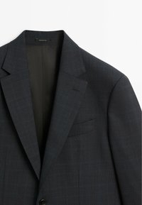 Mörk rutig kavaj med slag och en bröstficka samt knäppning framtill. Gjord av texturerat tyg med en slät innerfoder.