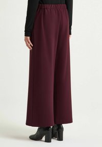 Pantaloni bordeaux a gamba larga con vita elastica; texture liscia; abbinati a stivali neri con tacco; design semplice, senza motivi visibili.