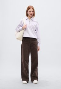 Ανοιχτό μωβ φούτερ με φερμουάρ και κεντημένη λεπτομέρεια, συνδυασμένο με καφέ παντελόνια φαρδιάς γραμμής και κρεμ τσάντα ταχυδρομείου, φορεμένο με λευκά αθλητικά παπούτσια.