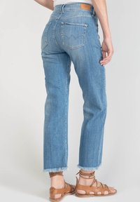 Jean en denim bleu clair avec bords effilochés, dotés d'un design classique à cinq poches et d'une étiquette en cuir sur la taille arrière.