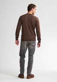 Suéter marrón de manga larga con cuello redondo, de tela texturizada, combinado con jeans grises y calzado marrón. Diseño simple y casual visto desde atrás.