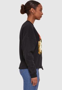 Czarny sweatshirt o luźnym kroju, z kolorowym graficznym wzorem na przodzie. Żebrowane mankiety i dół, zestawione z niebieskimi dżinsami.