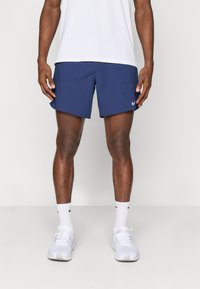 Ναυτικές αθλητικές βερμούδες με δύο μπροστινές τσέπες, ελαφρύ ύφασμα και μικρό λευκό λογότυπο Nike στο αριστερό πόδι. Φοριούνται με λευκό πουκάμισο και παπούτσια.