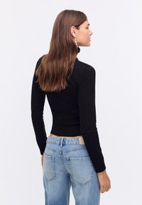 Zwarte longsleeve top met een aansluitend ontwerp en geribbelde textuur, gecombineerd met lichtblauwe high-waisted jeans.