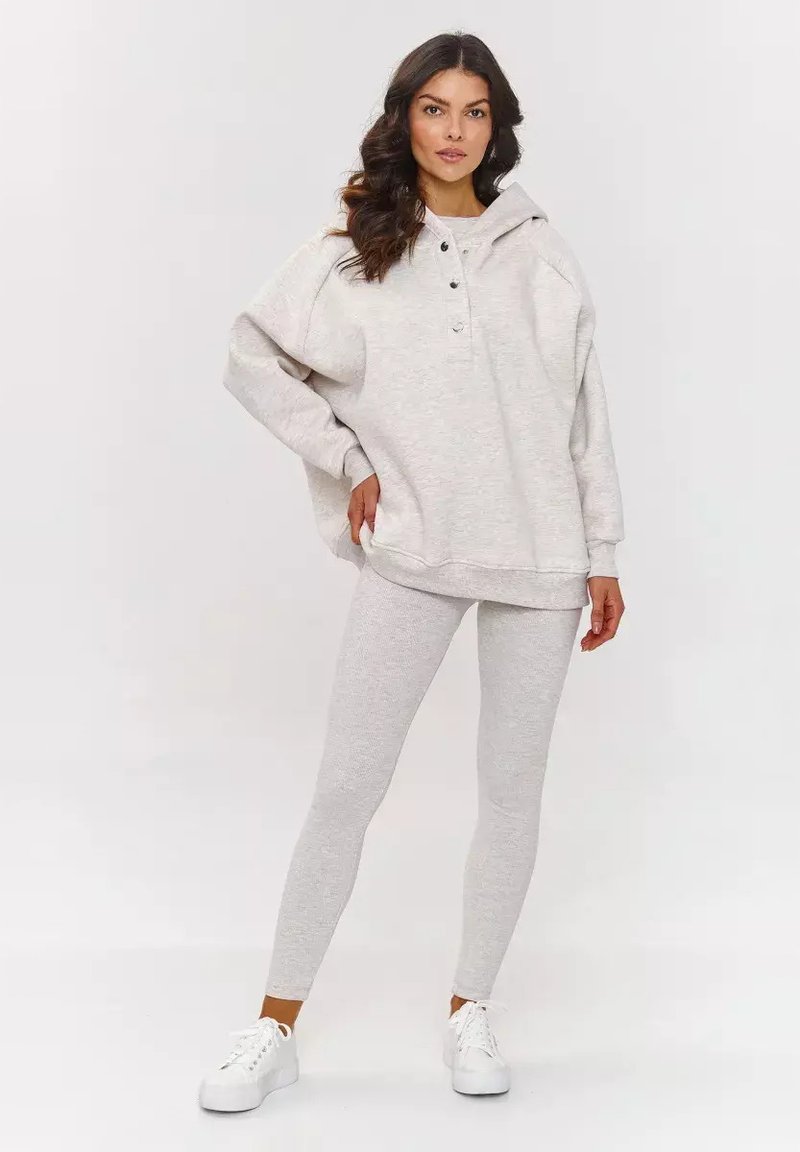 Jasnoszara, oversize'owa bluza z ribbowanym dołem i guzikami z przodu, w połączeniu z pasującymi jasnoszarymi legginsami. Wykonana z miękkiego, teksturowanego materiału.