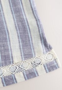 Gros plan sur un tissu rayé bleu et blanc avec une bordure en dentelle au crochet blanche présentant des motifs circulaires le long du bord.
