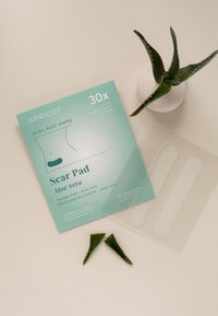 Aqua-groene verpakking gelabeld "Scar Pad Aloë Vera," met 30 herbruikbare pads, met twee aloë vera bladeren naast heldere plastic pleisters.