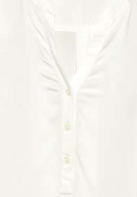Camicia bianca con un'abbottonatura dotata di cinque bottoni. Tessuto morbido e liscio con leggere pieghe vicino al collo e un design del colletto a forma di V.