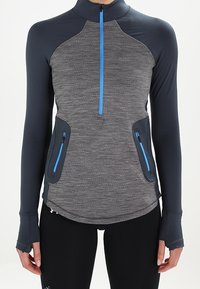 Szara bluzka z długim rękawem i półzapięciem z niebieskimi akcentami, teksturowana, z bocznymi kieszeniami na zamek i otworami na kciuki, zaprojektowana do aktywności fizycznej.
