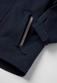 Marineblauwe jacket met een gladde textuur, ritszakken en verstelbare mouwmanchetten met klittenband, met een hedendaags ontwerp.