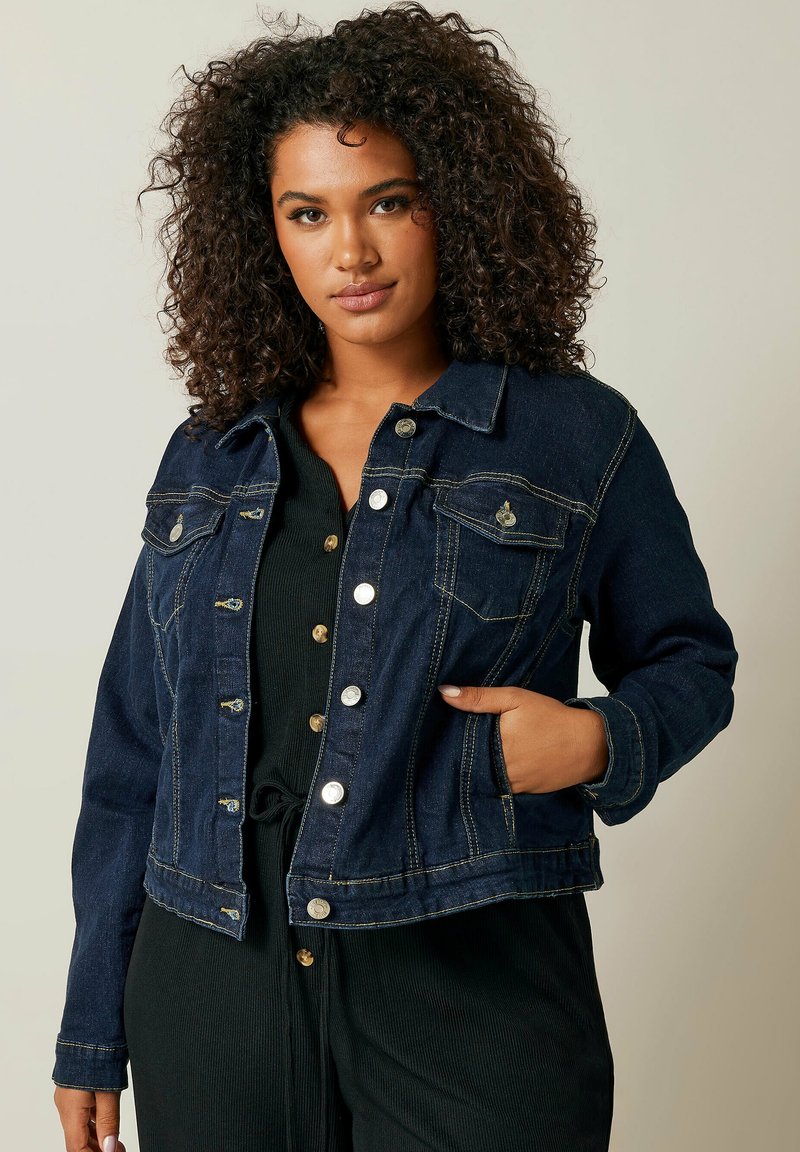 Tummansininen farkkutakki, jossa on hopeanväriset napit, kaksi rintataskua ja muotoiltu design. Raskas rakenne ja kontrastivärinen ommeltyyli.