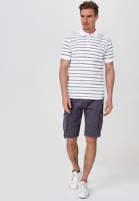 Vit polo med marinblå ränder, kombinerad med grå cargoshorts. Utsegningen kompletteras med vita sneakers. Enkelt, avslappnat design.