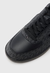 Black sneaker featuring a mix of textured fabric and smooth leather, with tonal patterns, lace-up design, and subtle logo on the side.
