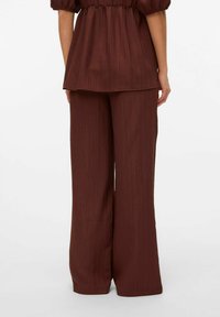 Haut peplum texturé marron avec manches bouffantes associé à un pantalon large assorti. Le tissu présente des rayures verticales subtiles.