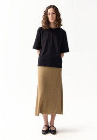 Czarna t-shirt z krótkim rękawem w połączeniu z długą, złotą, dzianinową spódnicą. Stylizacja charakteryzuje się luźnym krojem, a modelka nosi czarne płaskie buty.