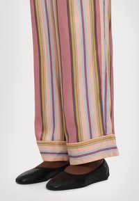 Stribede bukser med vide ben i pink, blå og gul med en afslappet pasform og en kant i kontrastfarver; parret med sorte flade sko.