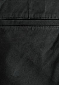 Vêtement en tissu noir avec une surface lisse et texturée ; présente des détails de couture et un design simple et uniforme sans motifs ni embellissements.
