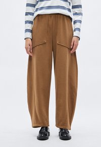 Bruine wijde sweatpants met twee voorzakken, elastische tailleband en een gladde textuur, gecombineerd met een gestreept shirt met lange mouwen en zwarte schoenen.